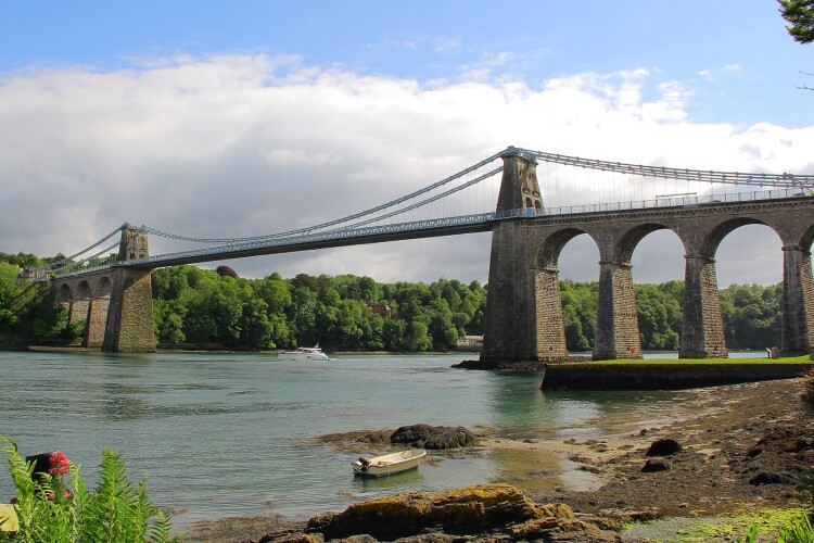 he Menai Suspension Bridge is a suspension bridge spanning the Menai Strait between the island of Anglesey and the mainland of Wales. Designed by Thomas Telford and completed in 1826, it was the world's first major suspension bridge. 